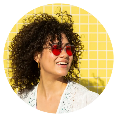 woman with curly black hair and red tinted sunglasses smiling