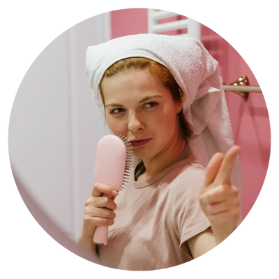 woman pointing in the bathroom holding a hairbrush and a towel wrapped around her hair